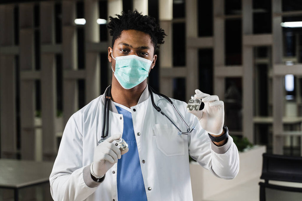 Черный врач с 3 дозами вакцины. Усилительная вакцинация. Африканский врач в медицинской маске держит в руках вакцины - Фото, изображение