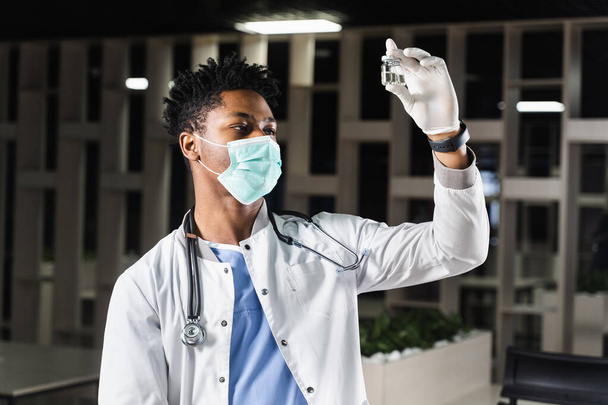 Fekete orvos két adag vakcinával. Emlékeztető oltás. Afrikai orvos orvosi maszkban tartja a vakcinákat a kezében. - Fotó, kép