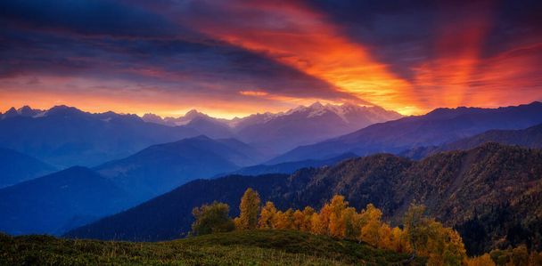 Φανταστικές κόκκινες ηλιαχτίδες με συννεφιασμένο ουρανό στους πρόποδες του βουνού. Ούσμπα. Δραματική πρωινή σκηνή. Τοποθεσία Upper Svaneti, Mestia, Georgia, Europe. Υψηλός Καύκασος. Ζεστό τονωτικό αποτέλεσμα. Ομορφιά κόσμος. - Φωτογραφία, εικόνα