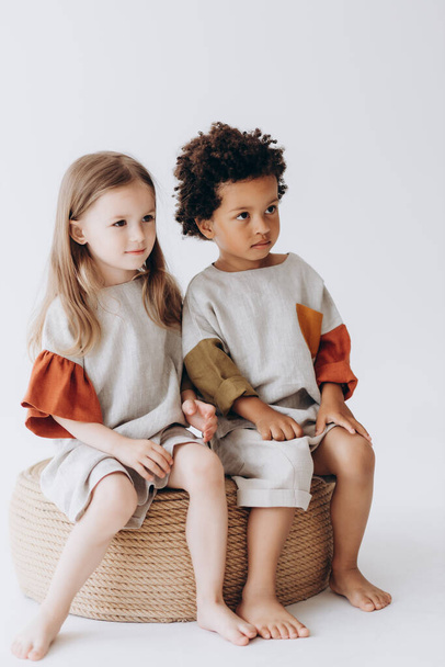 Photos of children having fun and posing for a photo in summer linen clothes in a photo studio. Dark-skinned boy and caucasian girl together in the photo - Fotó, kép