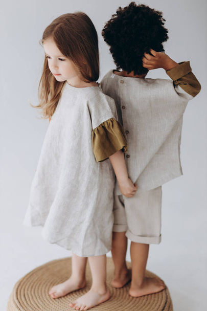 Photos of children having fun and posing for a photo in summer linen clothes in a photo studio. Dark-skinned boy and caucasian girl together in the photo - Photo, image