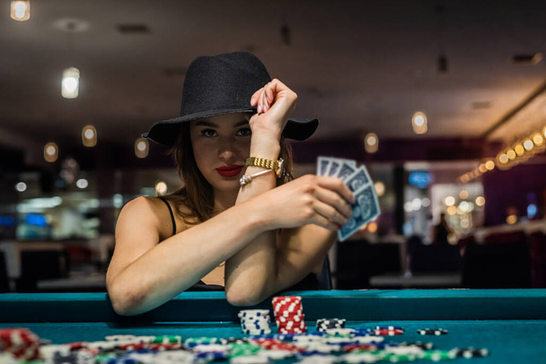 joven mujer atractiva jugando al póquer en la mesa con pilas de fichas y cartas. Celebrando - Foto, imagen
