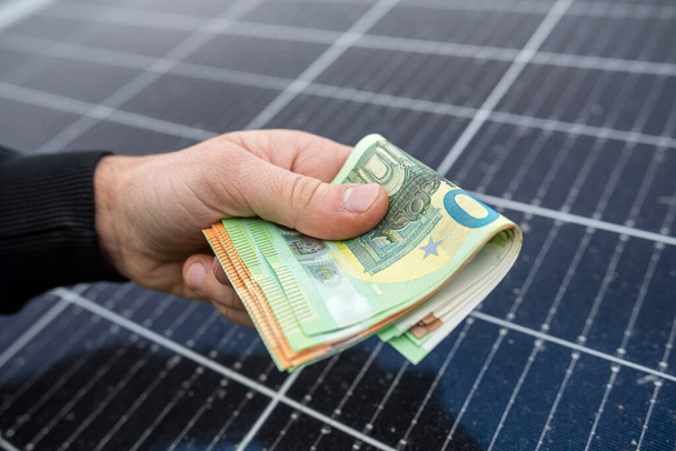 mooie jonge handen in het zwart houden een bedrag van euro in de voorkant van zonnepanelen. Concept groene elektriciteit - Foto, afbeelding