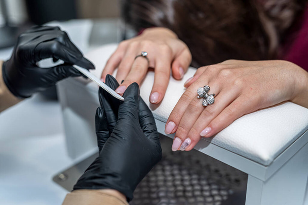 Eine Maniküre in speziellen Handschuhen sägt einem neuen Kunden während einer Epidemie die Nägel ab. Maniküre-Konzept. Kosmetologie-Konzept - Foto, Bild