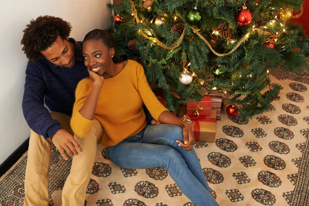 Weihnachten mit dem, den sie liebt. Aufnahme eines liebevollen jungen Paares, das neben einem Weihnachtsbaum sitzt. - Foto, Bild