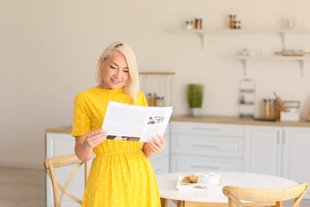 Beautiful mature woman reading newspaper in kitchen - Φωτογραφία, εικόνα