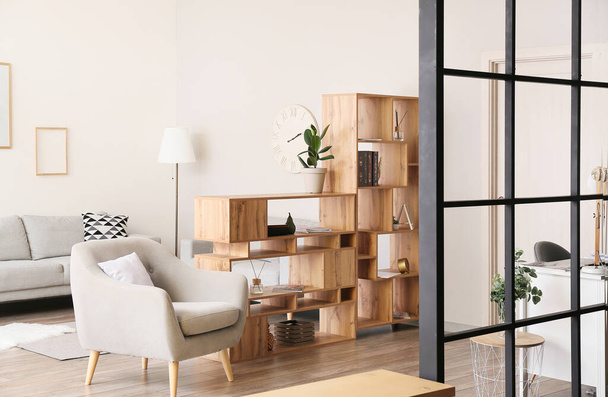 Интерьер светлой гостиной с деревянным шкафом и серым креслом - Фото, изображение