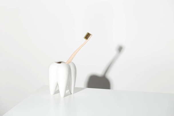 歯の形をしたスタンドで環境に優しい竹の歯ブラシ。意識的な消費と歯科ケアの概念. - 写真・画像