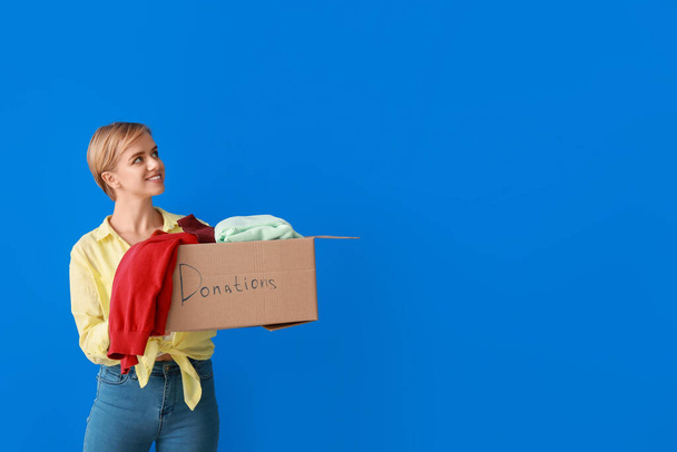 Mladá žena držení box s dárcovstvím oblečení na modrém pozadí - Fotografie, Obrázek