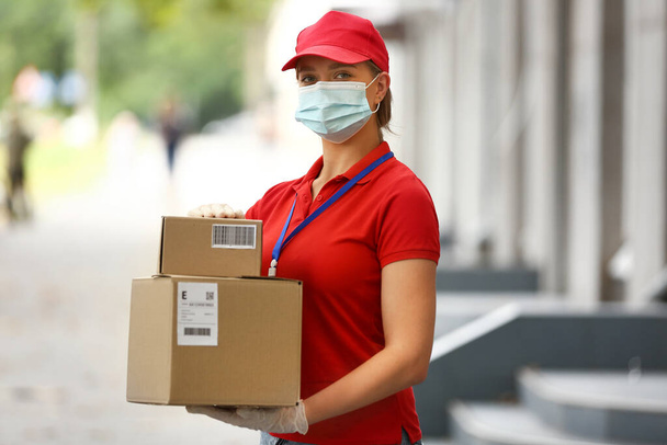 Курьер-женщина в медицинской маске и с посылками на улице - Фото, изображение
