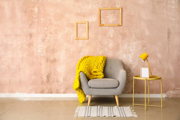 Stilvoller Couchtisch mit Lampe, Gestell und bequemen Sessel in der Nähe der Wand - Foto, Bild