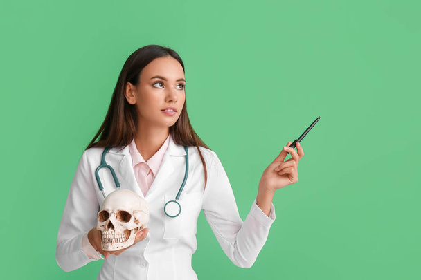 Vrouwelijke arts met menselijke schedel tonen iets op kleur achtergrond - Foto, afbeelding