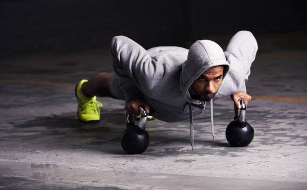 Focussed on his workout. Shot of a young man doing push-ups with kettle bell weights. - Φωτογραφία, εικόνα