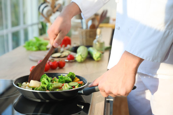 Male chef with spatula frying tasty vegetables in kitchen, closeup - Photo, Image