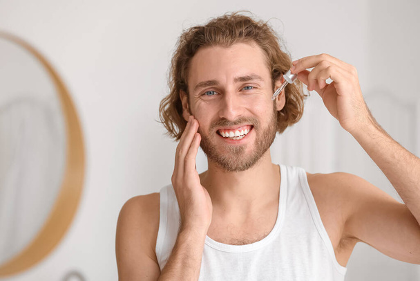 Junger Mann verwendet Serum zur Hautpflege im Badezimmer - Foto, Bild