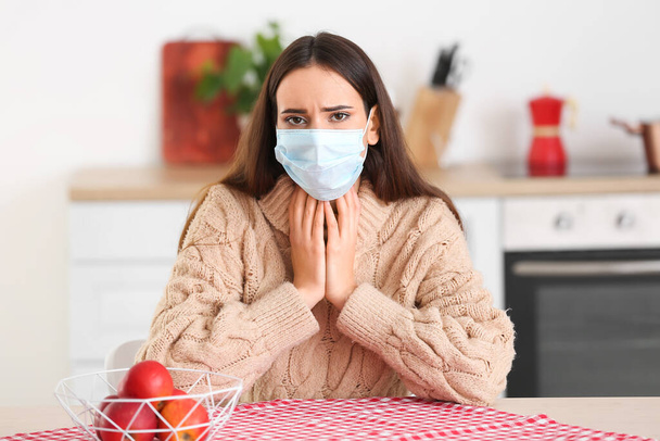 Jeune femme sous masque médical souffrant de maux de gorge à la maison - Photo, image