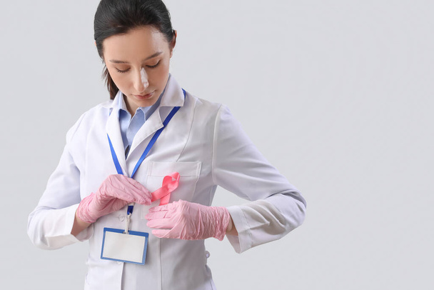 Oncóloga femenina con cinta rosa sobre fondo claro. Concepto de conciencia sobre el cáncer de mama - Foto, Imagen