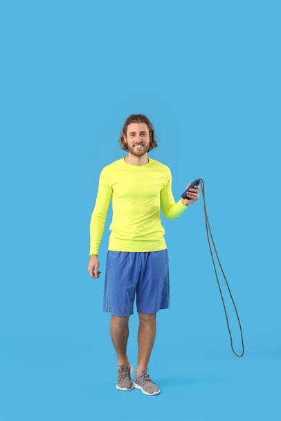 Sporty man with jumping rope on blue background - Foto, Imagen