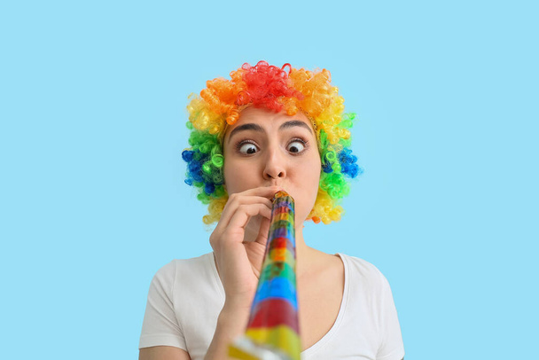 Grappige jonge vrouw met kleurrijke pruik en feestfluitje op blauwe achtergrond. 1 april dwaze dag viering - Foto, afbeelding