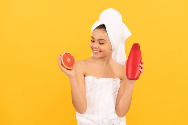 веселий підліток в рушнику з пляшкою шампуню з грейпфрутом на жовтому фоні
 - Фото, зображення