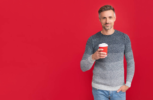 усміхнений придушений хлопець в светрі п'є каву на червоному фоні, вранці
 - Фото, зображення
