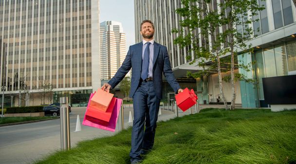 уверенный в себе предприниматель в иске, держащий сумку и подарочный коробок за пределами офиса, скидка. - Фото, изображение