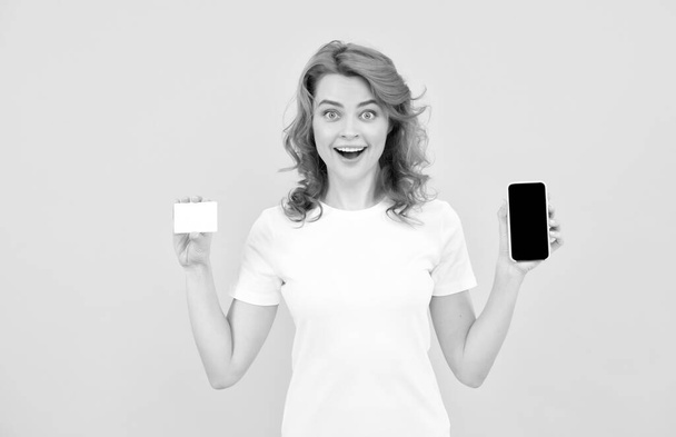 έκπληκτη κοπέλα δείχνει πιστωτική ή χρεωστική κάρτα και smartphone για να κάνει online αγορές, online ψώνια. - Φωτογραφία, εικόνα