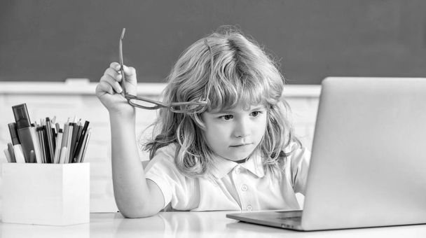 niño serio en gafas estudiar en línea en el aula de la escuela con el ordenador portátil, el día del conocimiento - Foto, imagen