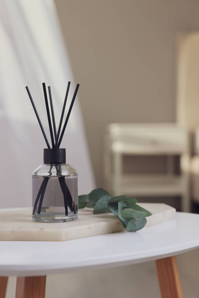Aromatic reed air freshener and eucalyptus branch on white table in room, space for text - Φωτογραφία, εικόνα