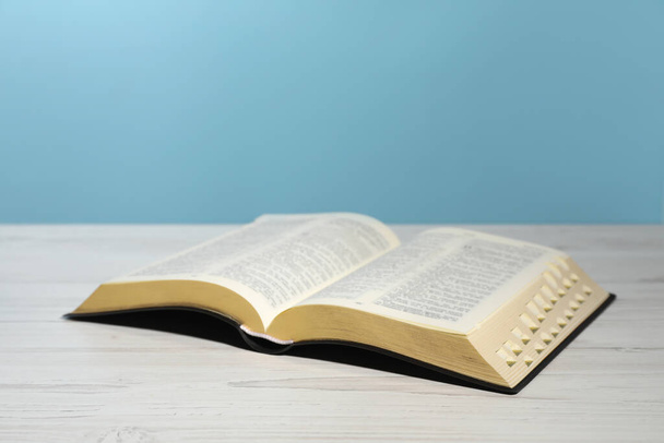 Open Bible on white wooden table against turquoise background. Christian religious book - Фото, изображение