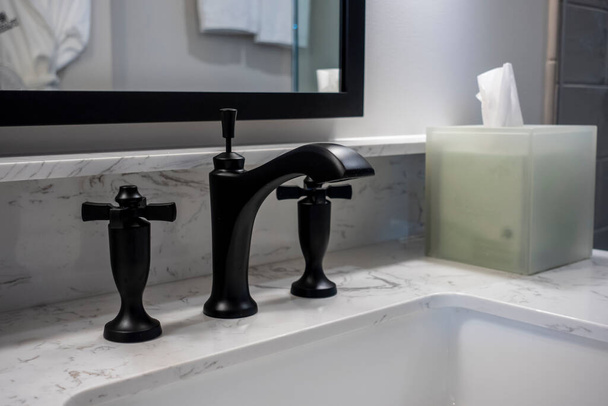 Angled, selective focus on a modern black bathroom sink faucet inside a high end, luxuery hotel - Photo, Image