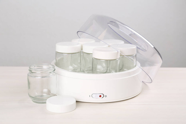 Moderne Joghurtmaschine mit leeren Gläsern auf weißem Holztisch - Foto, Bild