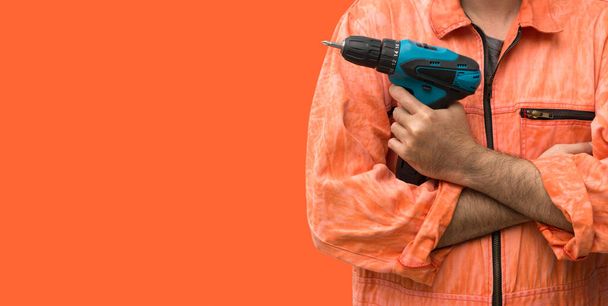 Chef mécanicien portant une robe uniforme orange tenant perceuse électrique bleue en face de fond orange. Portrait avec lumière de studio. - Photo, image