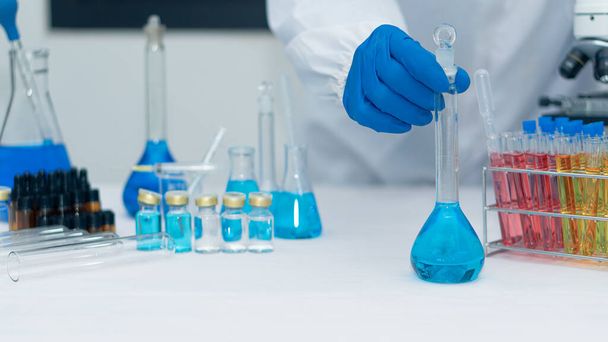 Scientist's hand tool holding a bottle with laboratory glassware in the background of a chemistry lab. Research and development concepts in science laboratories Medicine and Biotechnology - Foto, afbeelding