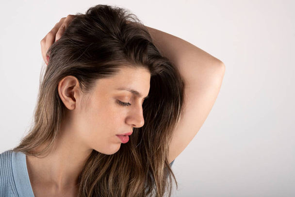Nuori nainen koskettaa hiuksiaan, vakava ja aistillinen ilme, puhtaalla taustalla - Valokuva, kuva