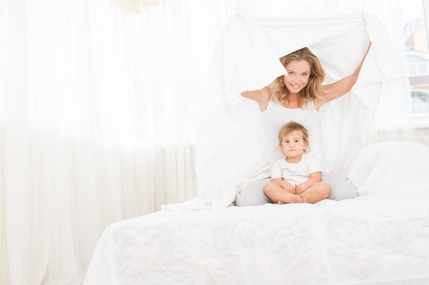 εσωτερική πορτρέτο του νεαρή ευτυχισμένη μητέρα και μωρό παιδί στο κρεβάτι με h - Φωτογραφία, εικόνα