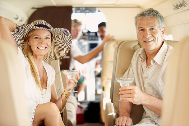 Летаю стильно. Снимок зрелой пары, сидящей на заднем сидении частного самолета и пьющей коктейли. - Фото, изображение