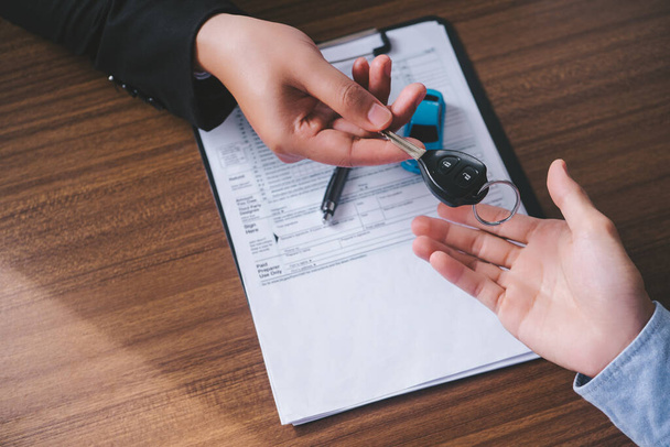 Autovermietung. Close up view Hand des Agenten gibt Autoschlüssel an Kunden nach unterschriebenem Mietvertrag Formular. - Foto, Bild