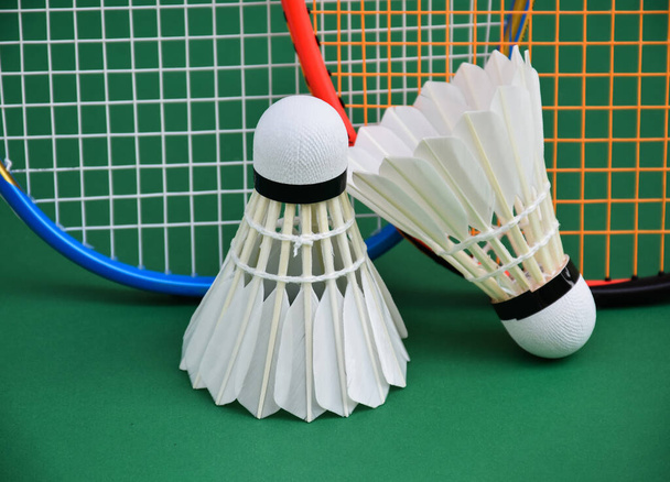 Cream white badminton shuttlecocks and rackets on green floor in indoor badminton court, copy space, concept for endurance exercise with indoor badminton sport. - Фото, изображение
