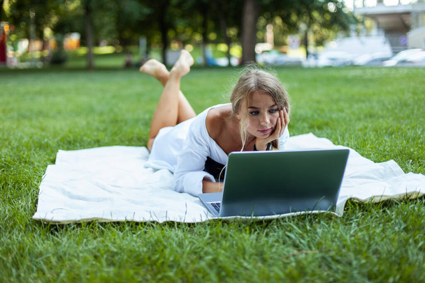 Όμορφη νεαρή γυναίκα που χρησιμοποιεί φορητό υπολογιστή σε καρό στο πάρκο - Φωτογραφία, εικόνα