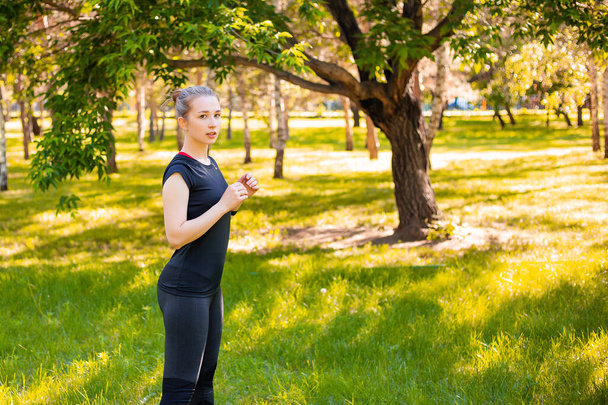 Una joven con uniforme deportivo se para en el parque lista para hacer ejercicio, copiar espacio. - Foto, Imagen