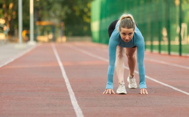 Young athletic woman runner in ready to start position at stadium - Photo, image