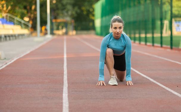 Young athletic woman runner in ready to start position at stadium - Photo, Image