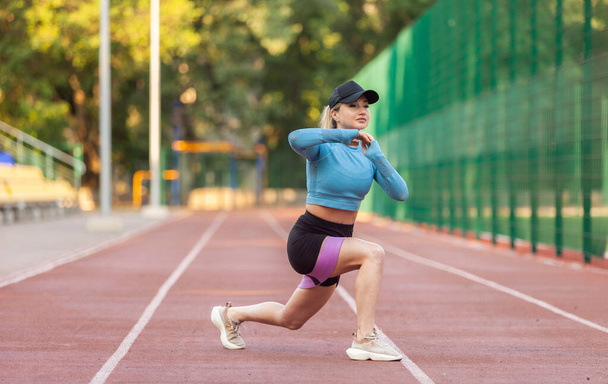 Atletische vrouw oefenen van lunges met fitness elastiekjes in het stadion - Foto, afbeelding