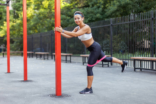 Giovane donna muscolare allena i muscoli con elastici fitness su un terreno di allenamento sportivo. Uno stile di vita sano. Fitness e bodybuilding. Formazione alla resistenza  - Foto, immagini