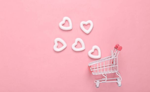 Bevásárlókocsi fehér szívvel, rózsaszín háttérrel. Kreatív elrendezés. Szerelem koncepció, boldog Valentin napot - Fotó, kép