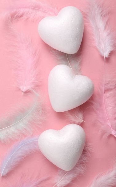 ピンクの背景にハートと柔らかい色の羽。愛の概念 - 写真・画像