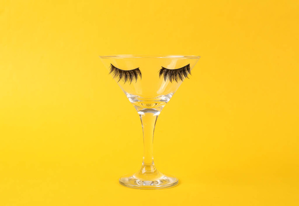 Cocktail glass with eyelashes on yellow background. Fresh idea. Minimal easter concept, creative layout - Photo, Image