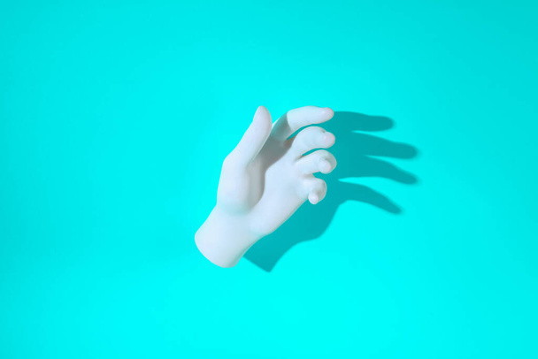 Mão de plástico branco sobre um fundo turquesa com uma sombra longa. Layout mínimo - Foto, Imagem