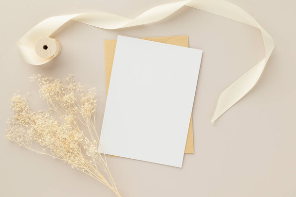 Carte de vœux vierge invitation Mockup 5x7 sur enveloppe marron avec fleurs séchées sur fond beige, pose plate, maquette - Photo, image